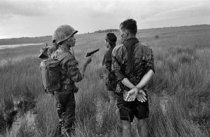 A South Vietnamese soldier holds a cocked pistol as he questions two suspected Viet Cong guerrillas captured in a weed-filled marsh in the southern delta region late in August 1962. The prisoners were searched, bound and questioned before being marched off to join other detainees. (AP Photo/Horst Faas)
